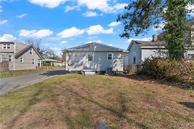 back of property with central air condition unit, a lawn, driveway, and fence