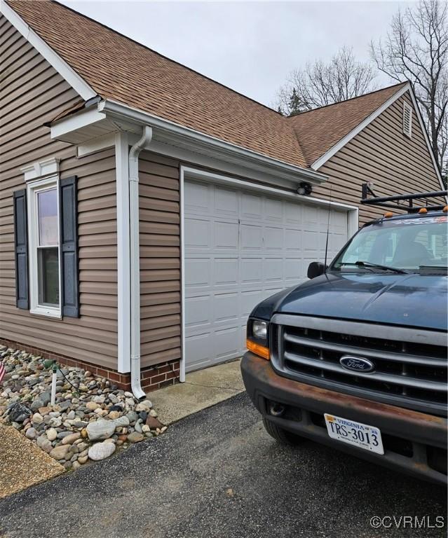 view of side of home featuring aphalt driveway, a garage, and roof with shingles