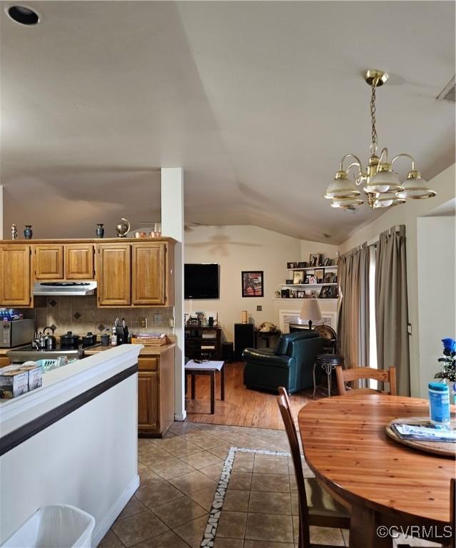 kitchen with dark tile patterned floors, under cabinet range hood, an inviting chandelier, decorative backsplash, and lofted ceiling