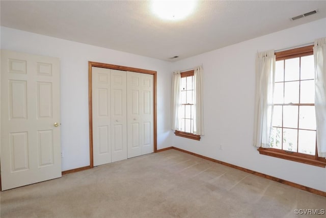 unfurnished bedroom with light carpet, visible vents, baseboards, and a closet