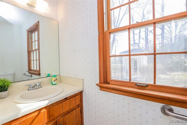 half bathroom with wallpapered walls, toilet, and vanity