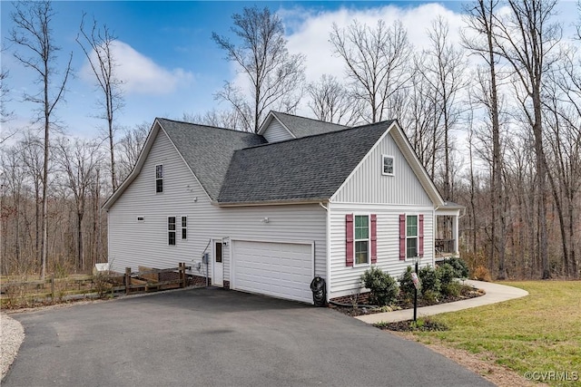 view of side of property with aphalt driveway, an attached garage, a lawn, and a shingled roof