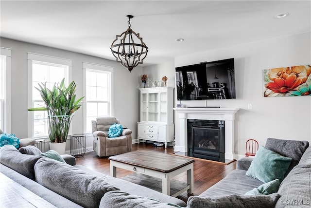 living room with a glass covered fireplace, recessed lighting, an inviting chandelier, and wood finished floors