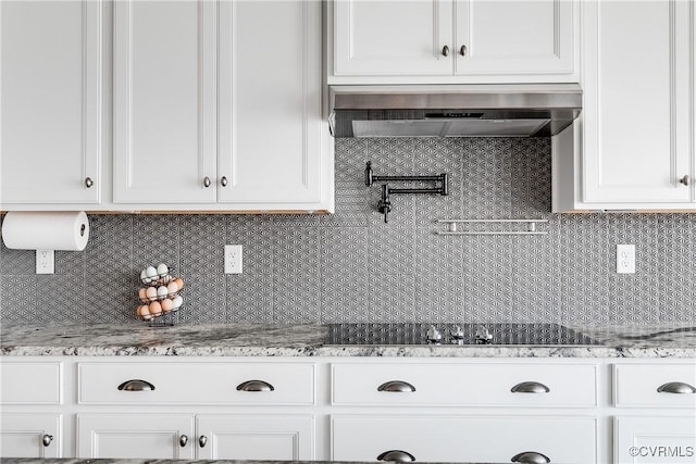 kitchen featuring black electric stovetop, wall chimney range hood, light stone countertops, decorative backsplash, and white cabinetry