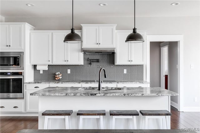 kitchen with appliances with stainless steel finishes, white cabinetry, dark wood-type flooring, and light stone countertops