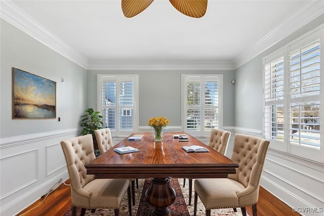 dining room with a wainscoted wall, ornamental molding, a ceiling fan, and wood finished floors