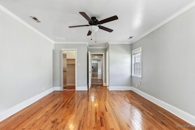 unfurnished bedroom with light wood finished floors, visible vents, a walk in closet, baseboards, and ornamental molding