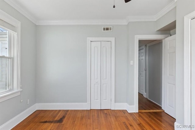 unfurnished bedroom with wood finished floors, visible vents, baseboards, a closet, and crown molding