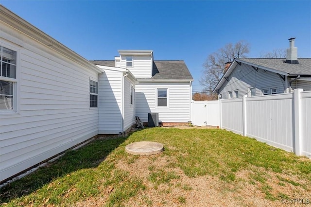 rear view of house with central air condition unit, a lawn, and fence