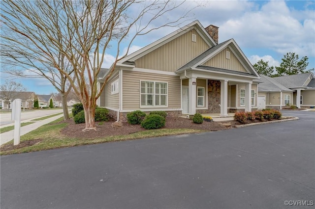 craftsman-style house with a porch, a chimney, a garage, stone siding, and driveway