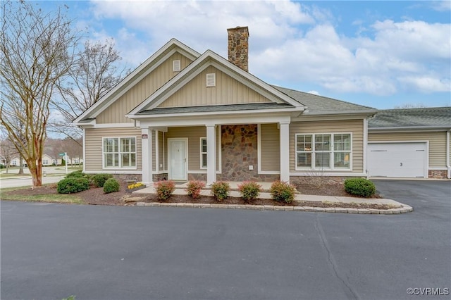 craftsman house with board and batten siding, a chimney, driveway, stone siding, and an attached garage