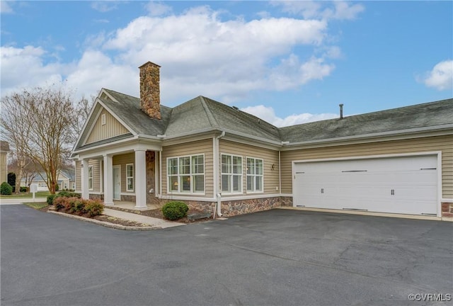 view of front of property with aphalt driveway, stone siding, roof with shingles, an attached garage, and a chimney