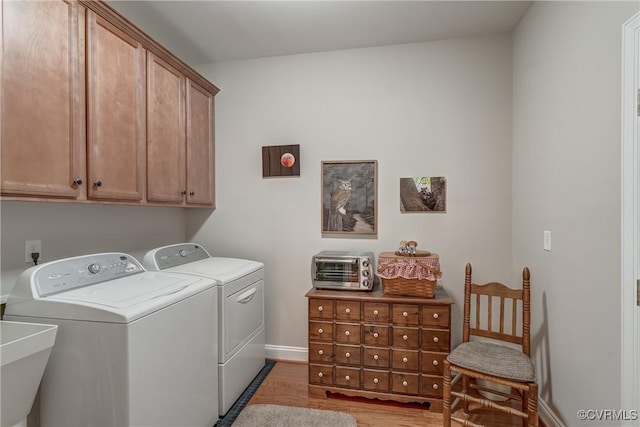 washroom featuring washing machine and clothes dryer, cabinet space, baseboards, and light wood-style floors