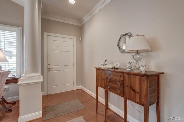 foyer entrance featuring baseboards, wood finished floors, ornate columns, and ornamental molding