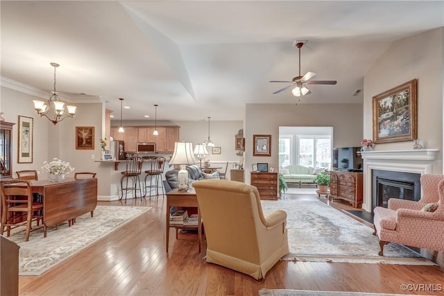 living area featuring a glass covered fireplace, light wood-style flooring, ceiling fan with notable chandelier, and vaulted ceiling