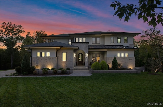 prairie-style home featuring a standing seam roof, a lawn, brick siding, and metal roof