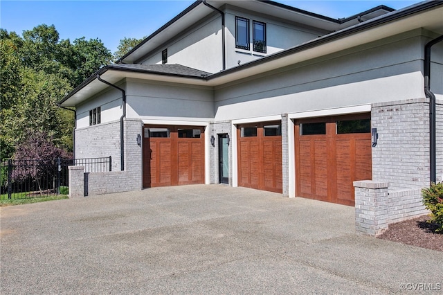 view of property exterior featuring stucco siding, brick siding, concrete driveway, and fence