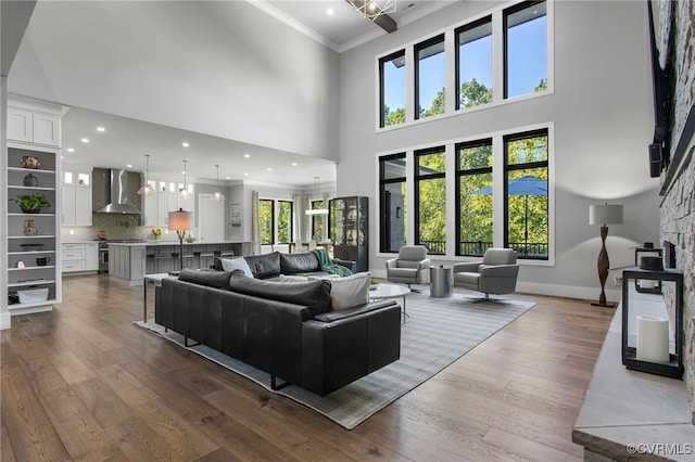 living room featuring baseboards, a high ceiling, recessed lighting, ornamental molding, and dark wood-type flooring