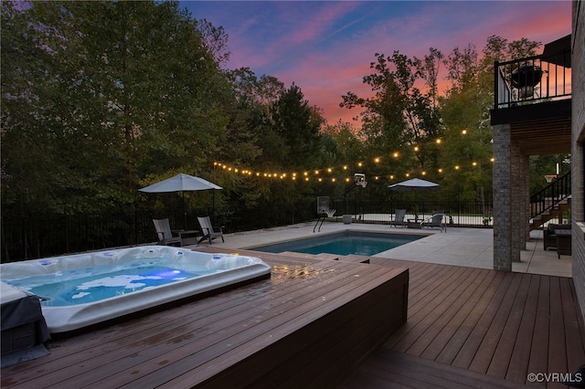 pool at dusk with a wooden deck, a patio, hot tub deck surround, and a fenced backyard