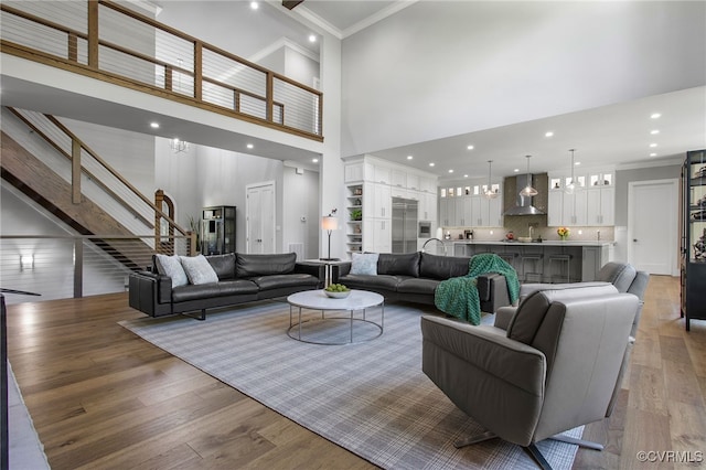 living area featuring a notable chandelier, ornamental molding, wood finished floors, a high ceiling, and stairs