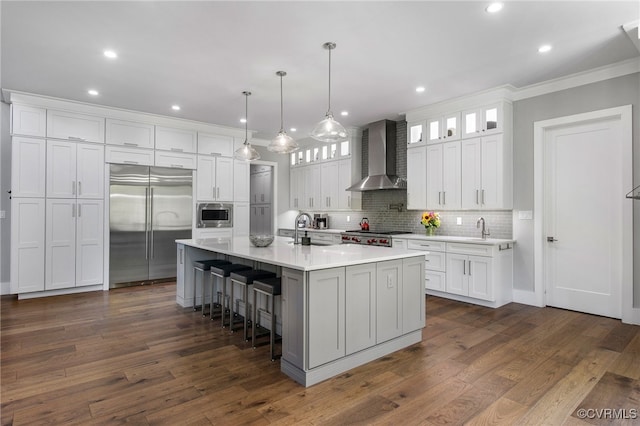 kitchen featuring built in appliances, white cabinets, wall chimney range hood, and a sink