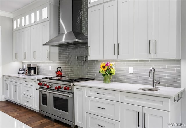 kitchen with a sink, double oven range, wall chimney exhaust hood, and white cabinetry