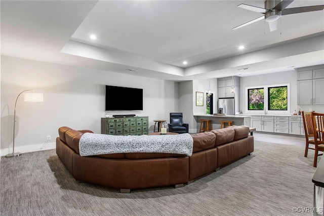 living area with baseboards, light colored carpet, recessed lighting, a raised ceiling, and a ceiling fan