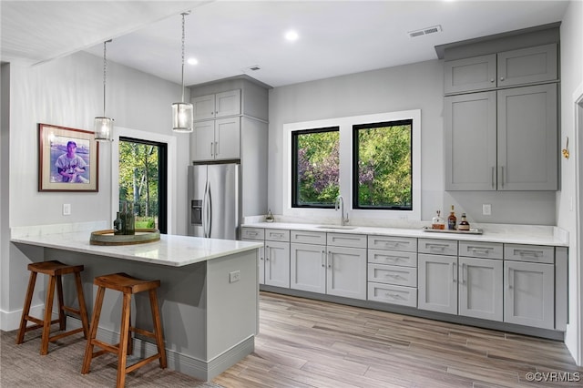 kitchen with visible vents, a kitchen bar, gray cabinetry, stainless steel refrigerator with ice dispenser, and a sink