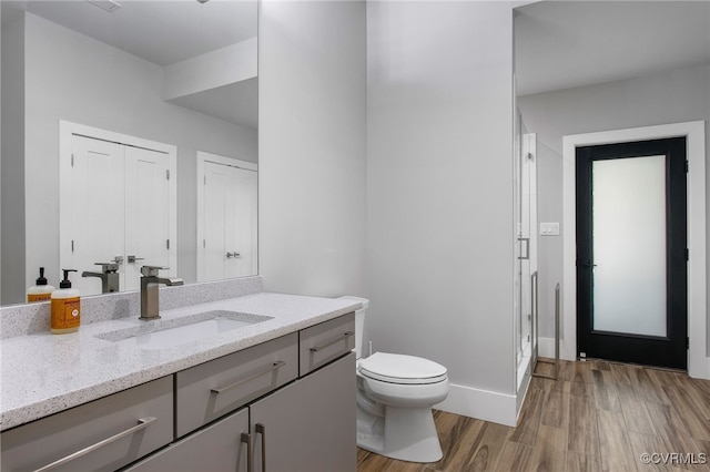 bathroom featuring vanity, wood finished floors, baseboards, a shower stall, and toilet