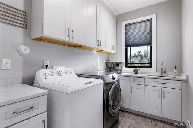 laundry room with cabinet space, separate washer and dryer, light wood-style flooring, and a sink