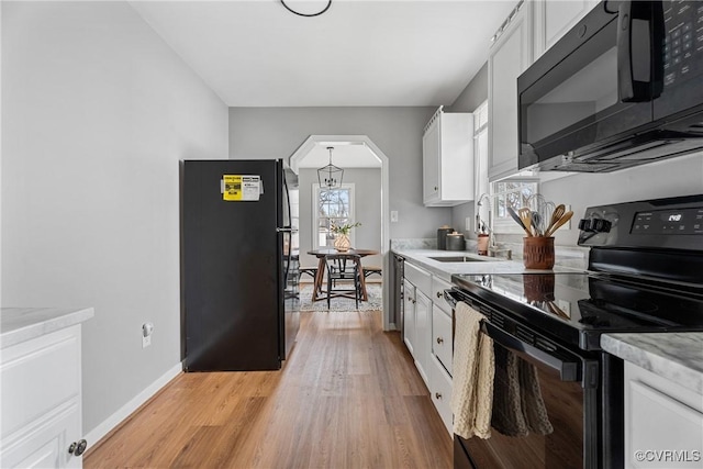 kitchen featuring black appliances, a sink, arched walkways, light wood-style floors, and white cabinets