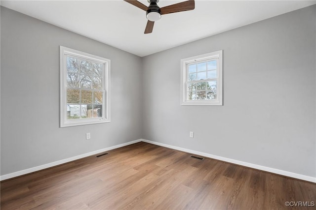 spare room with visible vents, plenty of natural light, baseboards, and wood finished floors