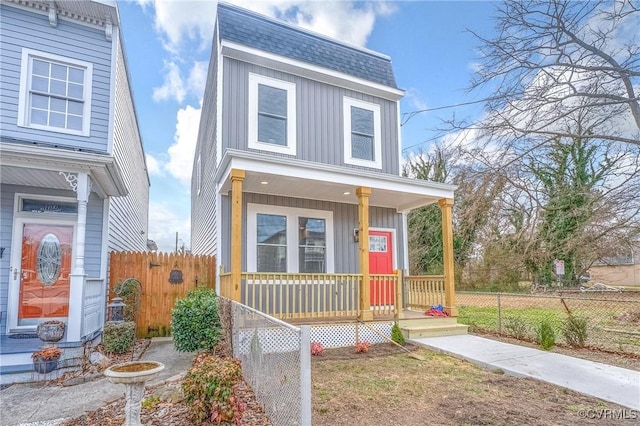 view of front of home featuring board and batten siding, fence, a porch, roof with shingles, and mansard roof