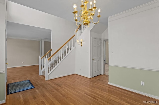 entrance foyer featuring a notable chandelier, wood finished floors, crown molding, baseboards, and stairs