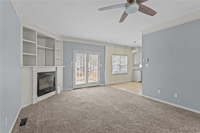 unfurnished living room featuring visible vents, a glass covered fireplace, crown molding, baseboards, and light colored carpet