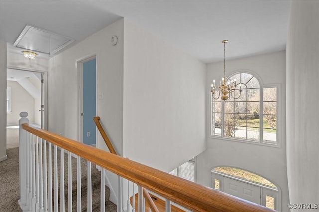 corridor featuring an upstairs landing, carpet floors, attic access, and an inviting chandelier