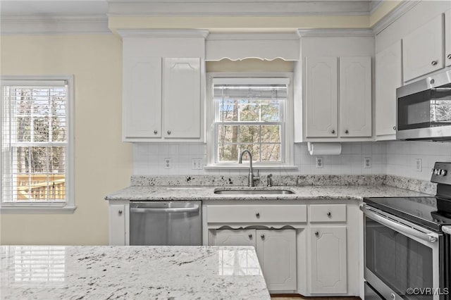 kitchen with ornamental molding, a sink, appliances with stainless steel finishes, white cabinetry, and backsplash