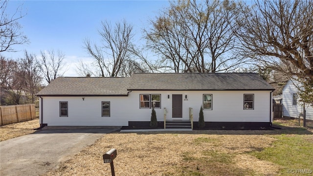 ranch-style home with roof with shingles, a front lawn, and fence