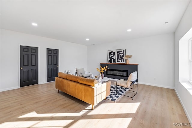 living area with a glass covered fireplace, light wood-style flooring, and recessed lighting