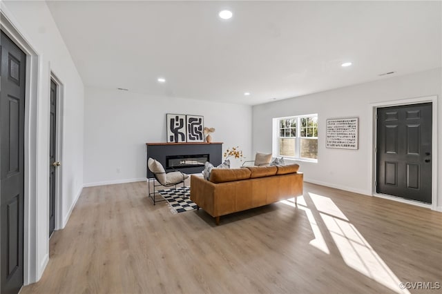 living room with a glass covered fireplace, light wood-style flooring, recessed lighting, and baseboards