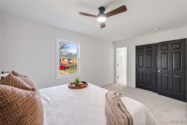 bedroom with a closet, light colored carpet, baseboards, and a ceiling fan