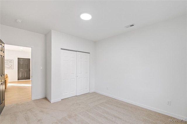 unfurnished bedroom with visible vents, baseboards, a closet, and light carpet