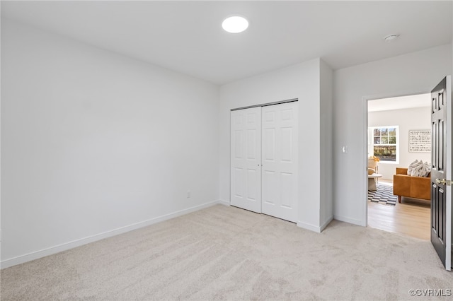 unfurnished bedroom featuring baseboards, a closet, and light carpet