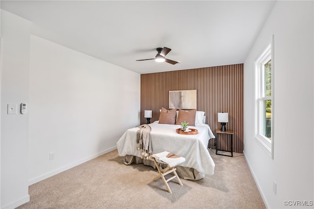 bedroom featuring ceiling fan, an accent wall, baseboards, and carpet floors