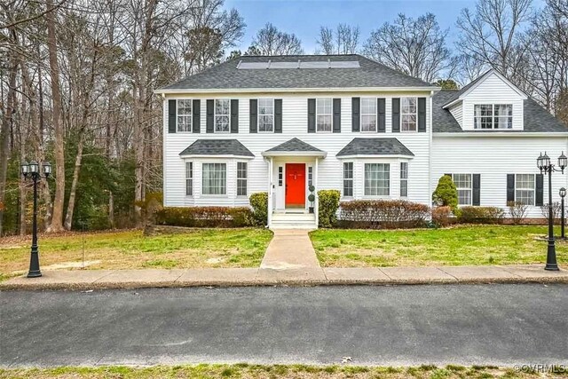 colonial inspired home featuring a shingled roof and a front yard