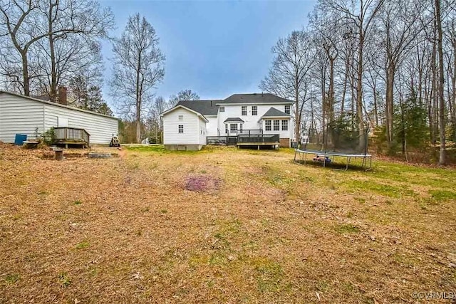 back of property with a wooden deck, a trampoline, and a yard