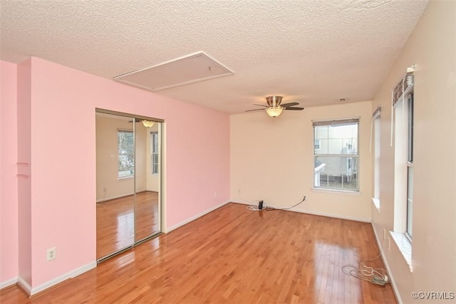spare room with a textured ceiling, a healthy amount of sunlight, attic access, and light wood-type flooring