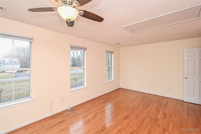 empty room with a ceiling fan, attic access, light wood finished floors, and a textured ceiling