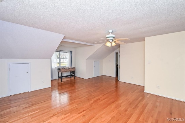 additional living space with a ceiling fan, a textured ceiling, vaulted ceiling, and light wood-type flooring