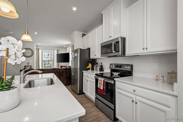 kitchen with a sink, open floor plan, white cabinetry, appliances with stainless steel finishes, and light countertops